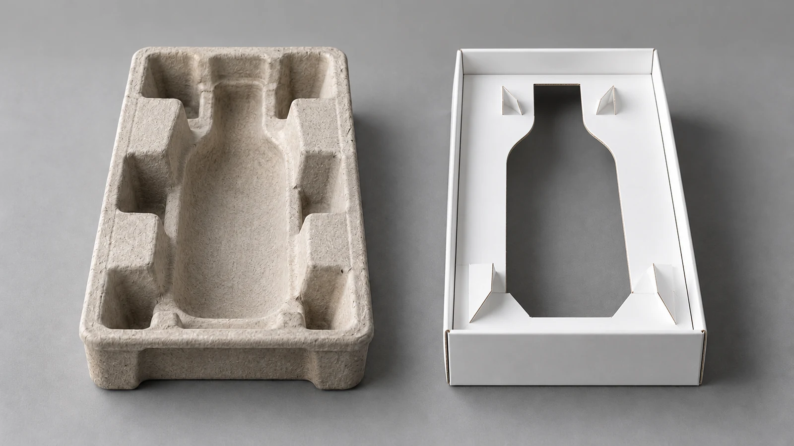 A natural moulded fibre insert and a white die-cut folded paperboard insert side by side, both empty, on a grey tabletop.