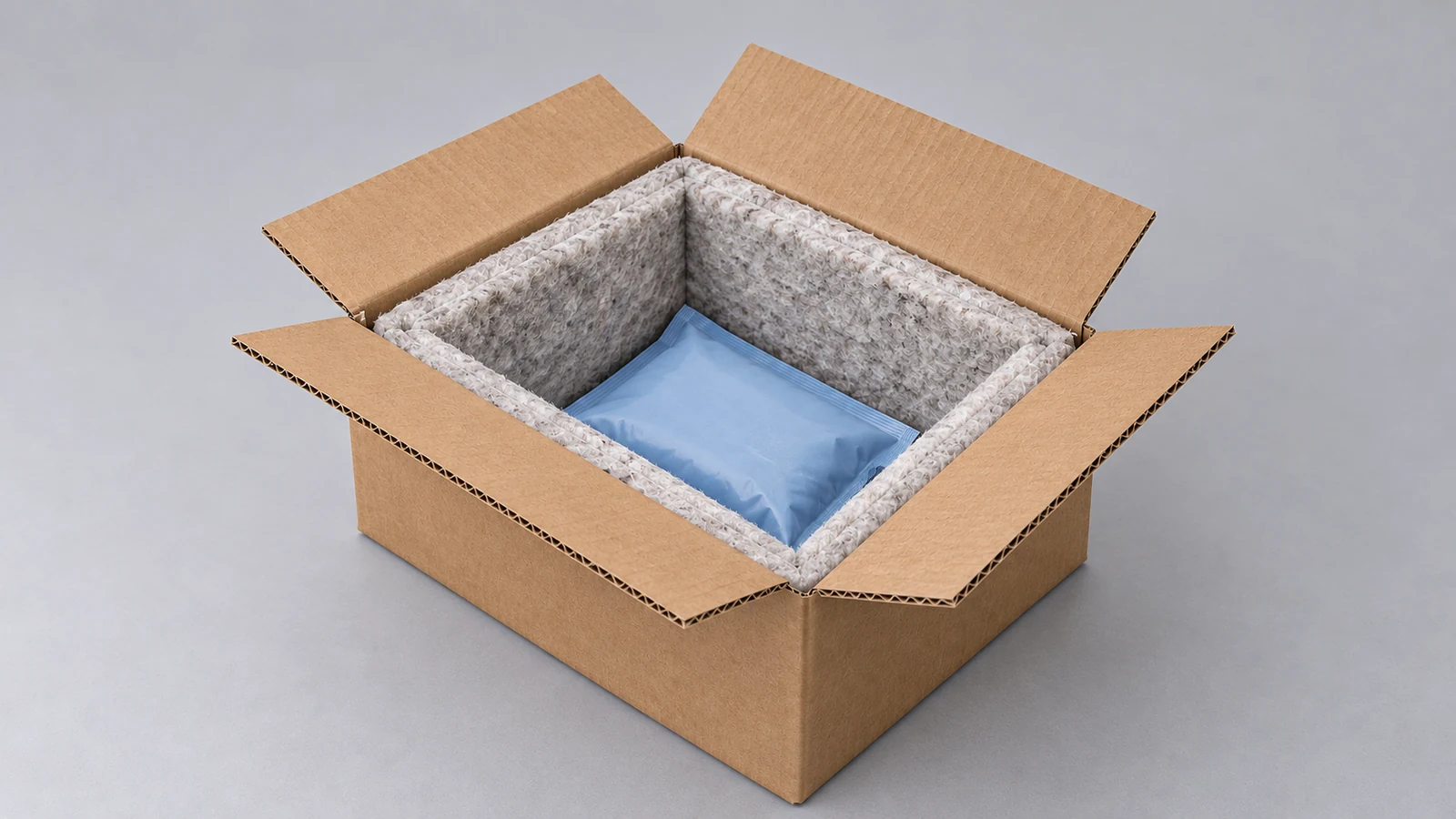 An open kraft shipping box with thick paper-fibre insulation and one blue coolant pouch on a grey tabletop.