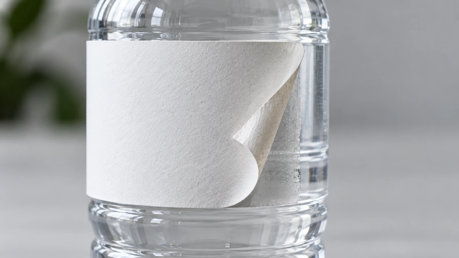Close-up of a white paper label partly lifted from a clear plastic bottle, revealing its edge and adhesive area.
